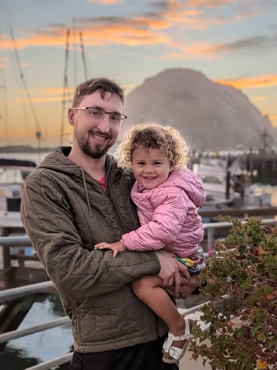 Jade's husband holding their daughter at a harbor at sunset